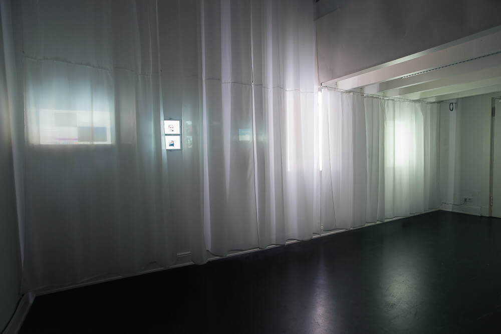 A dark room with illumniated shapes behind an opaque curtain.