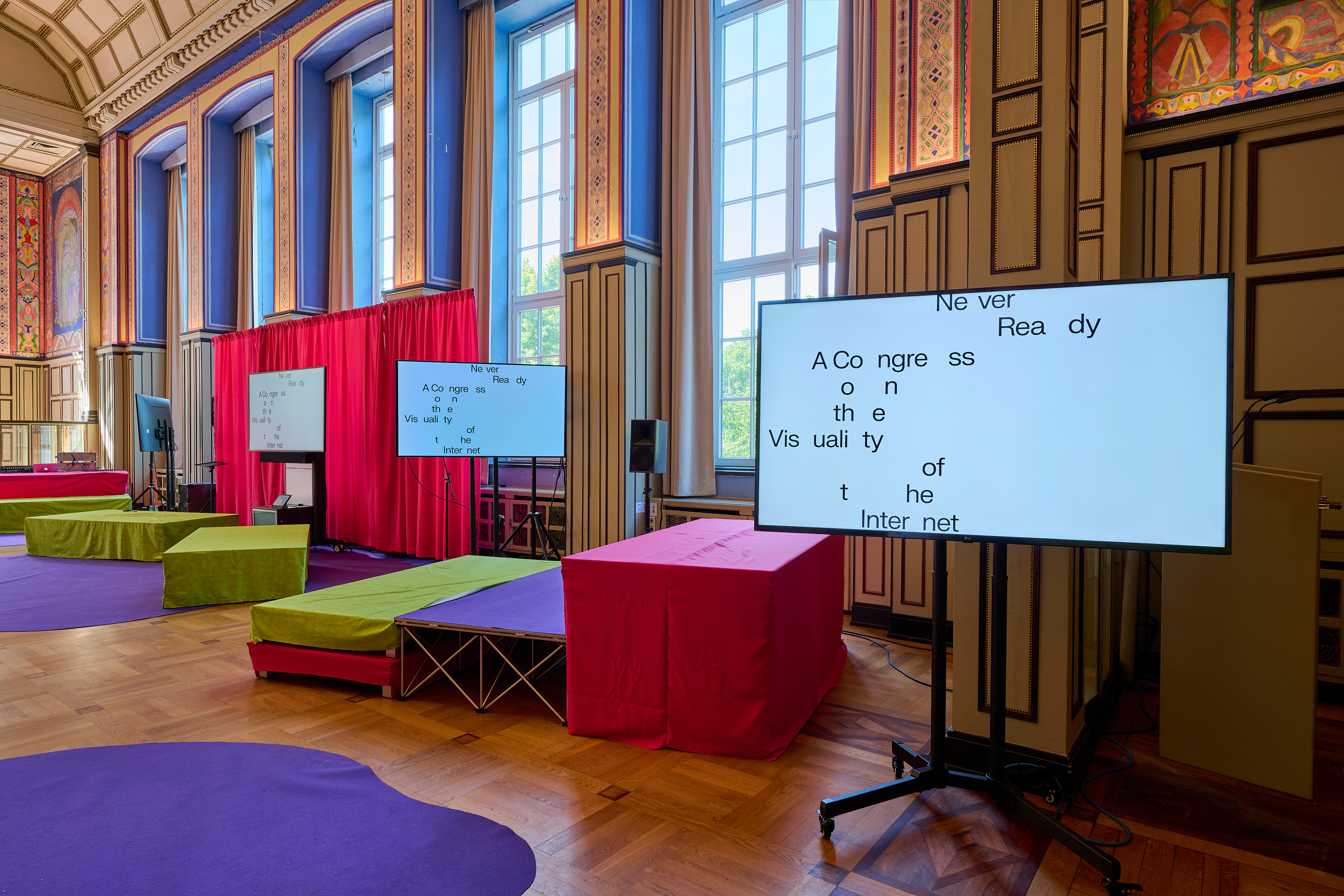 Big screens in a colorful decorated room, showing black airy letters on white ground.