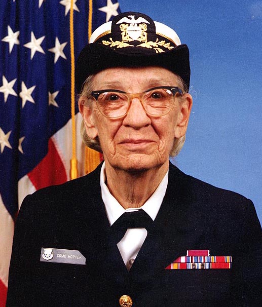 Portrait of an old female person, wearing an official uniform with coloured badges.A US american flag in the background.